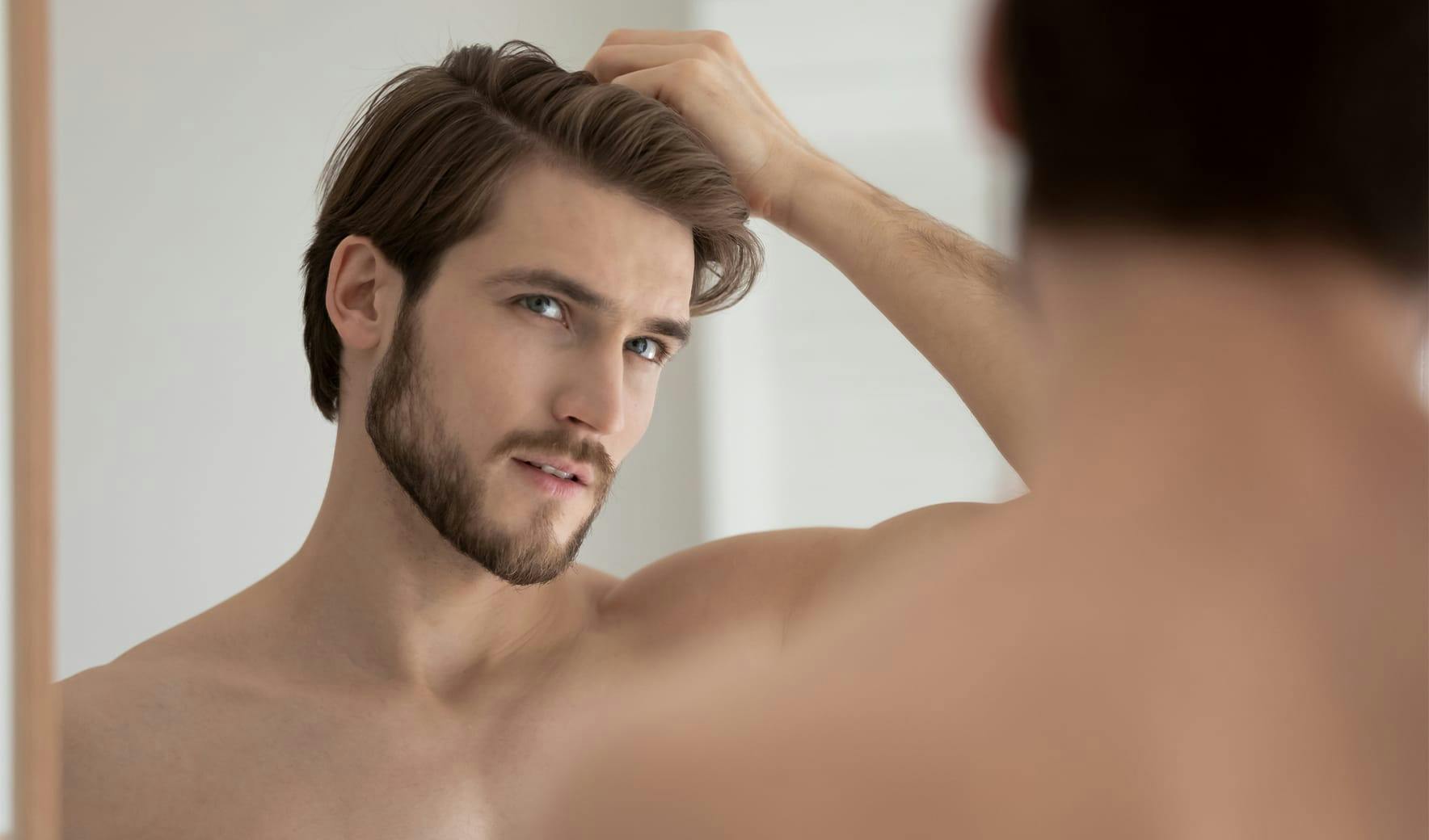 man looking in mirror rubbing hair
