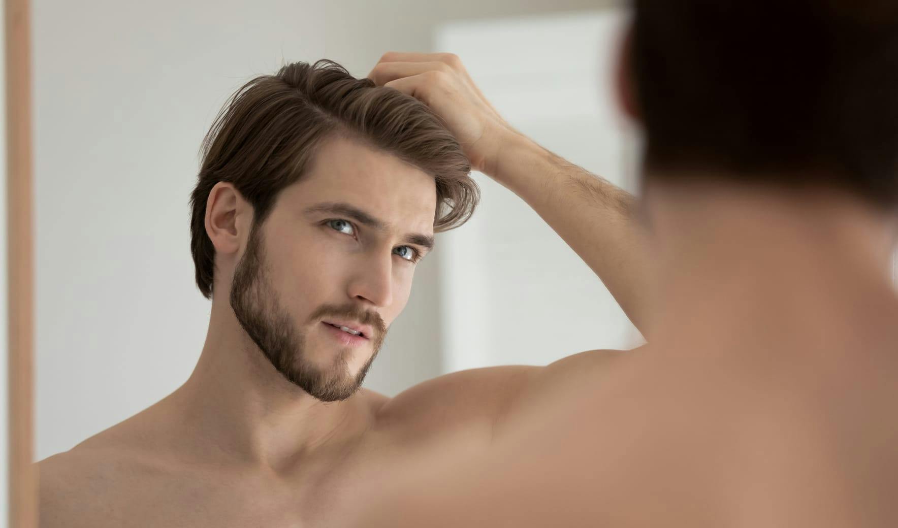 man looking in mirror rubbing hair