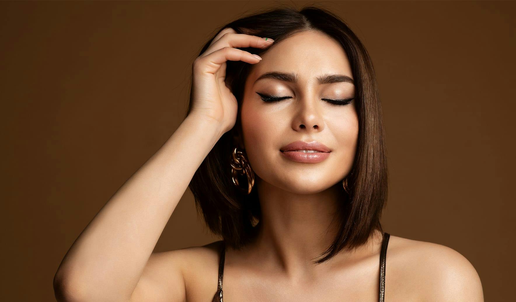 woman with short brown hair touching head