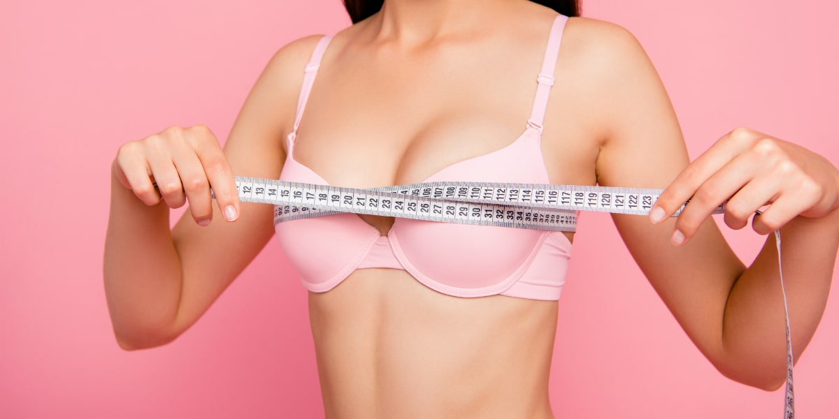 girl in bra measuring chest size line with tape isolated over pink background