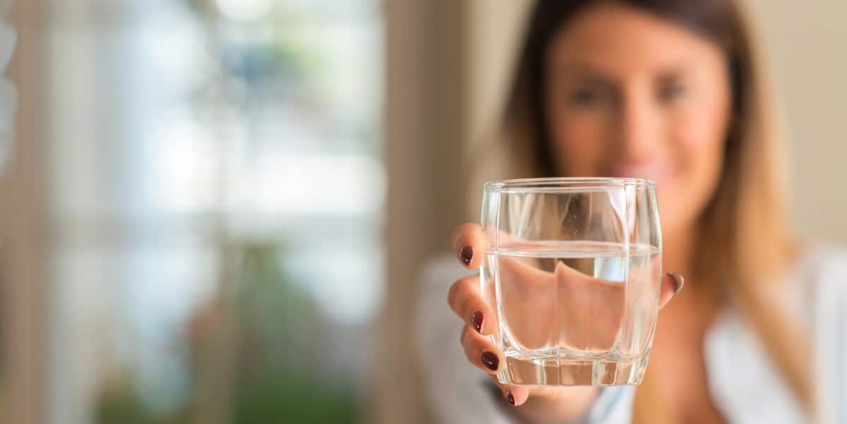 Beautiful young woman smiling while holding a glass of water at home.