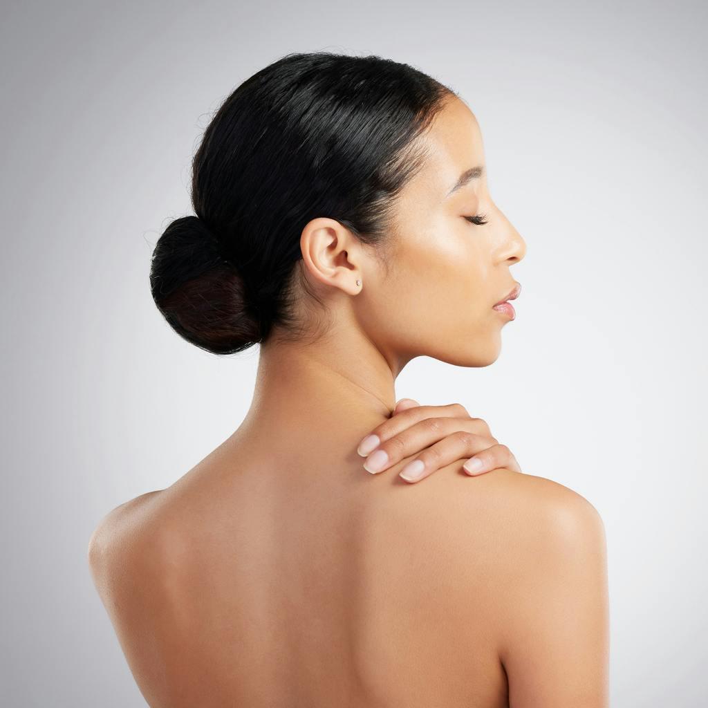 Woman with smooth, even-toned skin seen from behind with her hand on her shoulder, representing laser scar treatment in Fort Lauderdale
