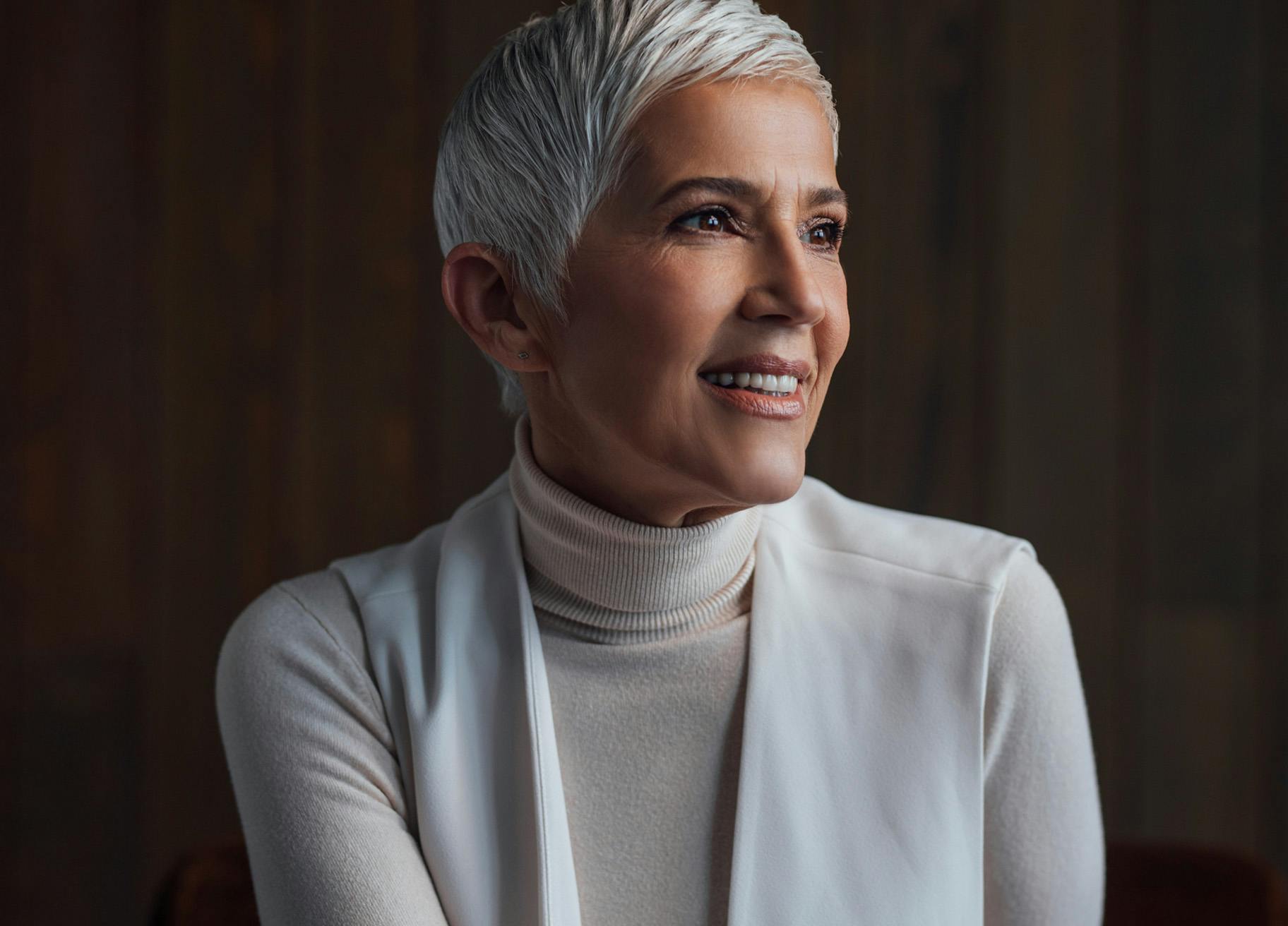 Woman with short grey hair wearing a white turtleneck top