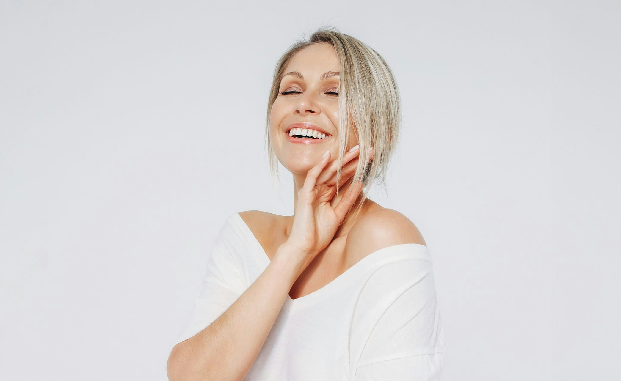 smiling woman with eyes closed accenting face with hand