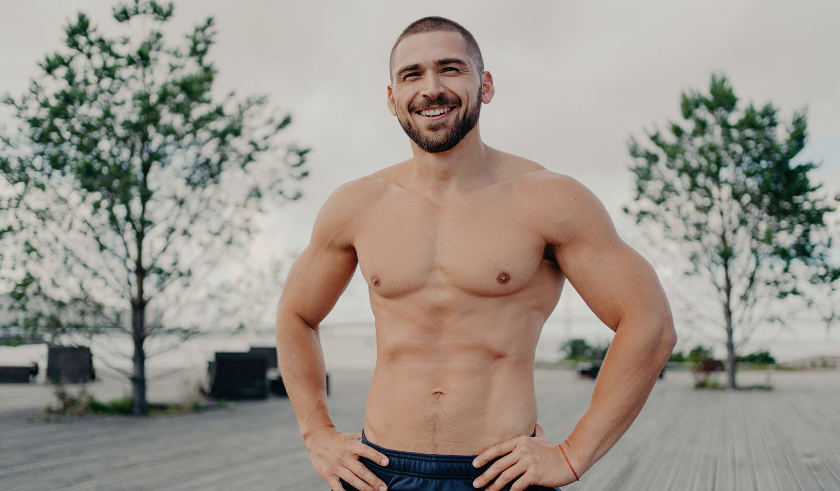 athletic man standing by trees with shirt off