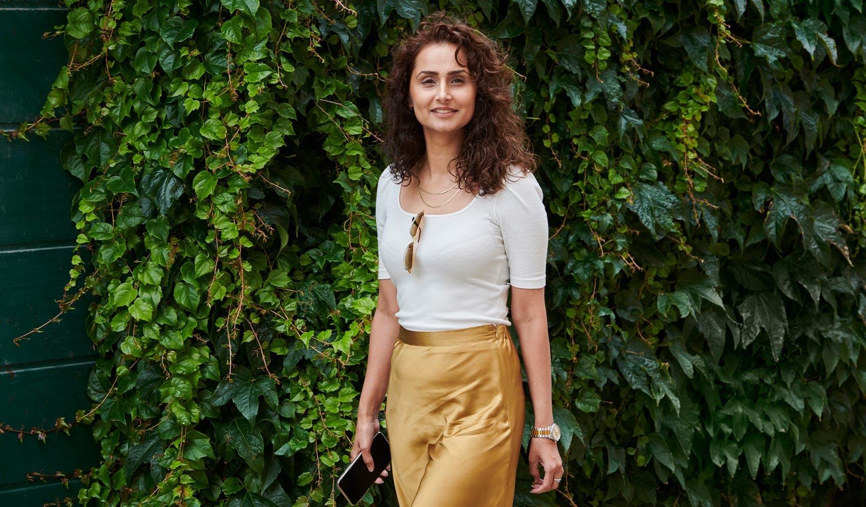 Woman smiling and standing next to overgrown wall of plants