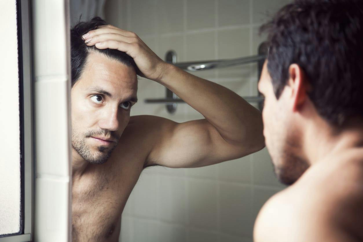 man looking at his hairline in the mirror