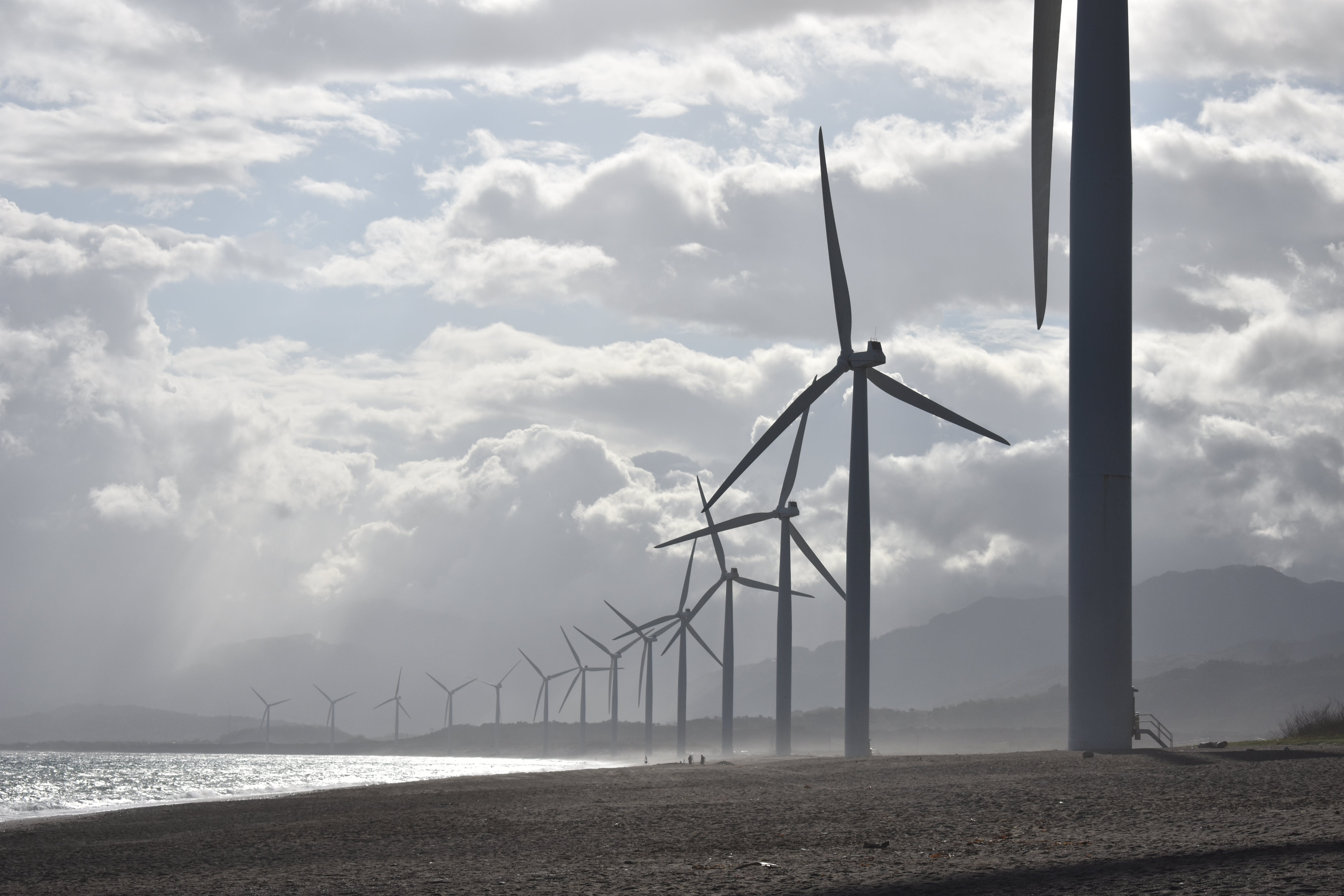 A line of wind turbines along a shoreline in cloudy weather.