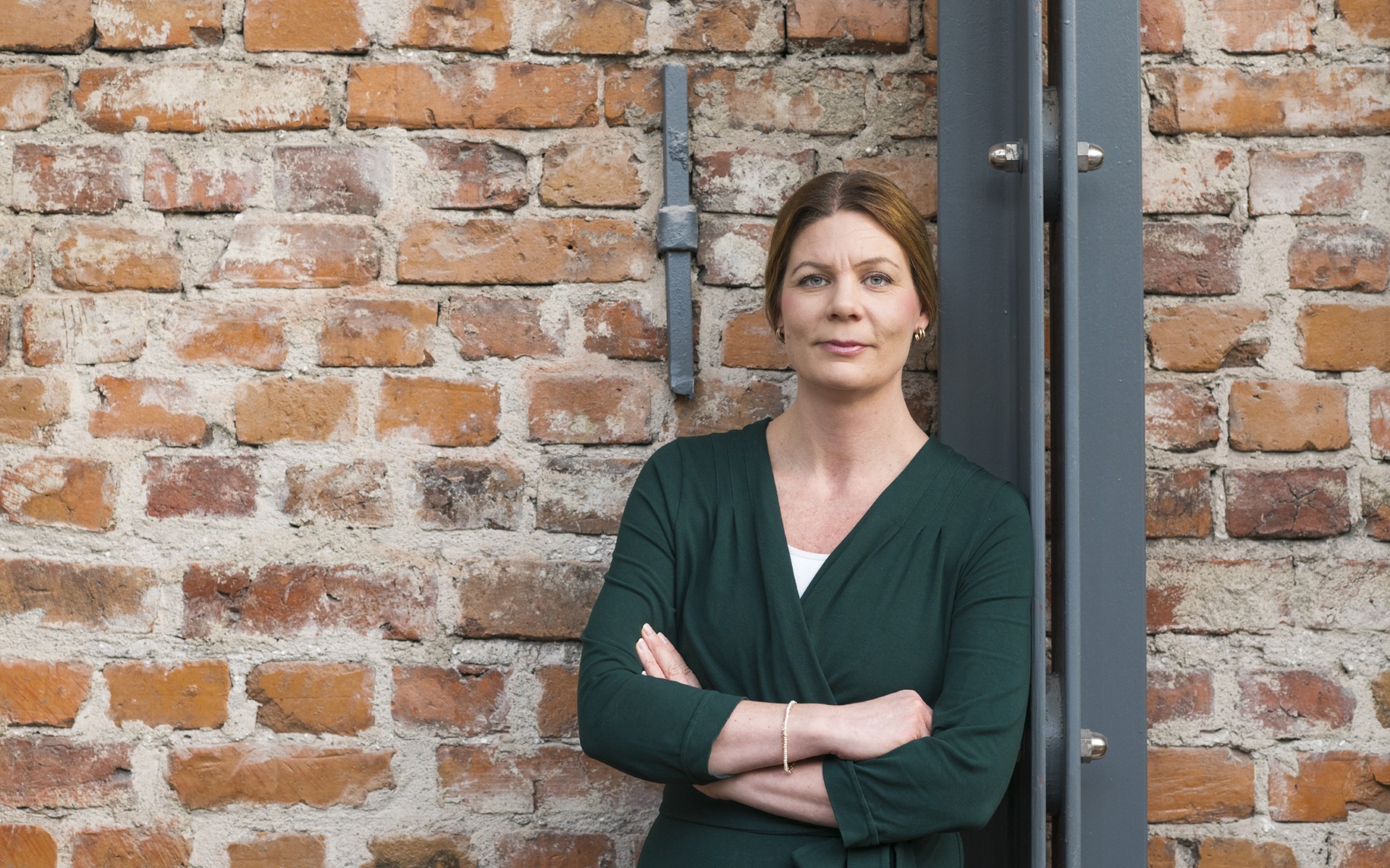 Ellen Einebrandt, vd Återvinningsindustrierna Brunhårig kvinna i grön klänning som står lutad med armarna i kors mot tegelvägg.