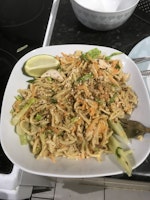 A bowl of bang bang chicken noodles with a wedge of lime