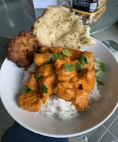 Bowl of butter chicken, served with rice, naan and an onion bhaji