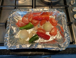 A roasting tray of green chillies, tomatoes, onion and garlic