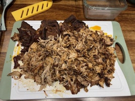 A chopping board of pulled pork being pulled apart