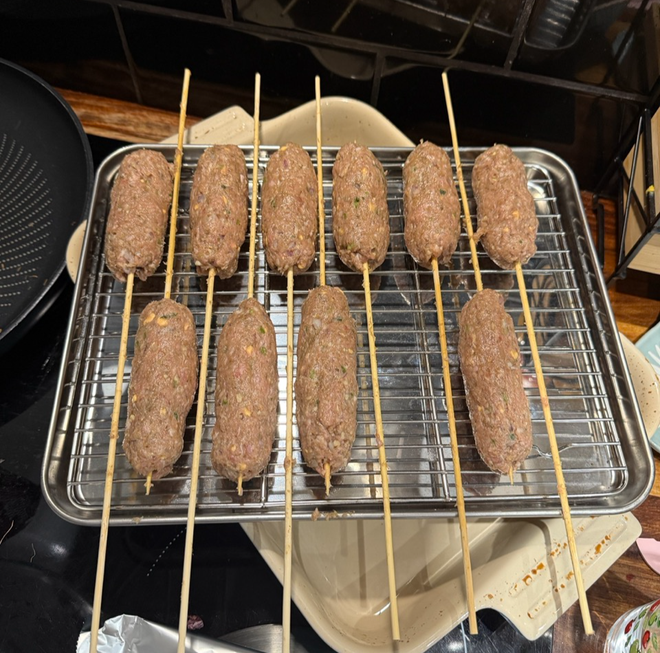 A baking tray of Lamb Sheekh Kabab with skewers through them ready to be cooked