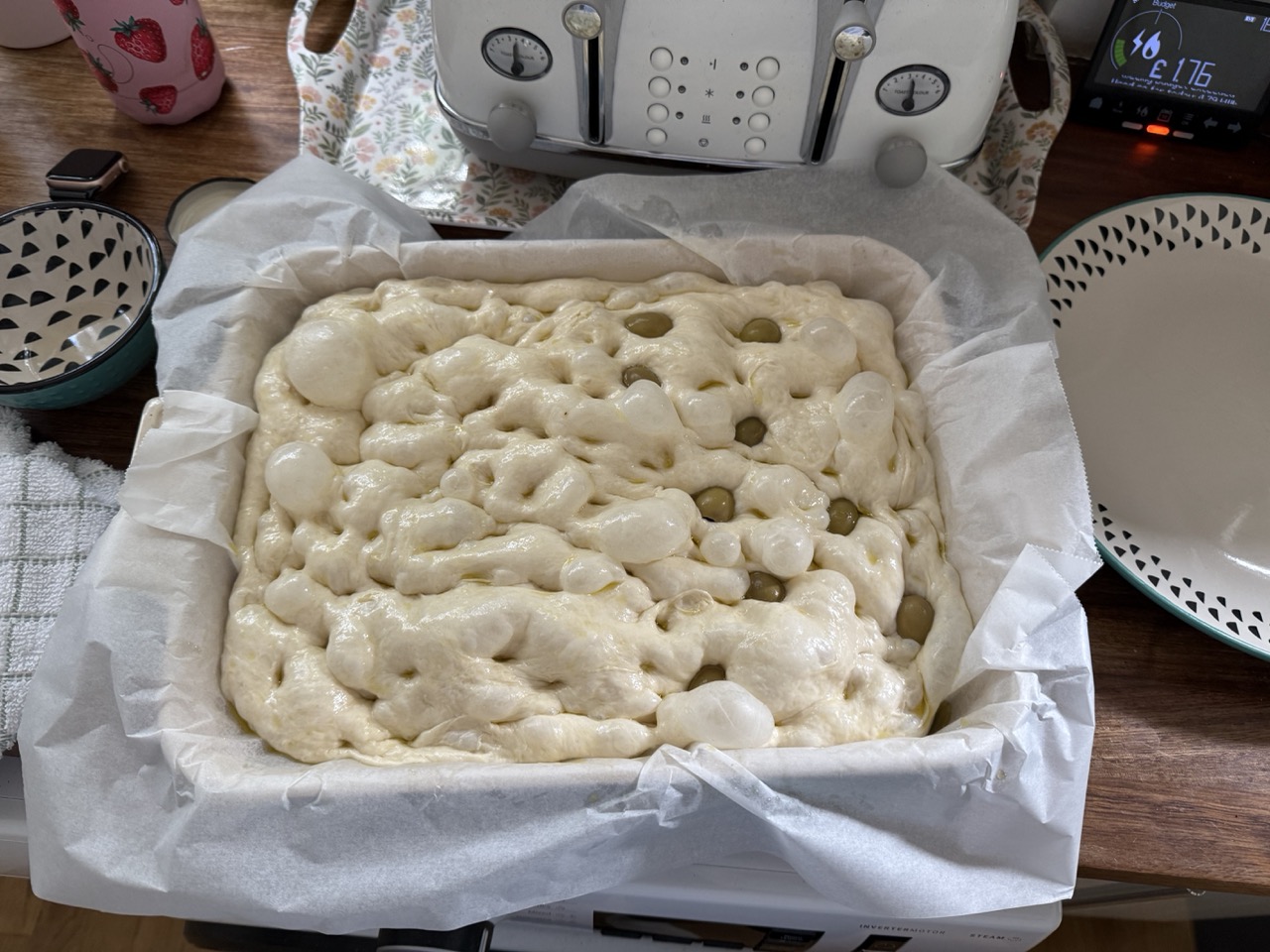 A baking tray of foccacia dough, drizzled with olive oil and topped with olives, ready to be baked