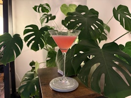 A glass of cosmopolitan in a martini glass in front of a plant