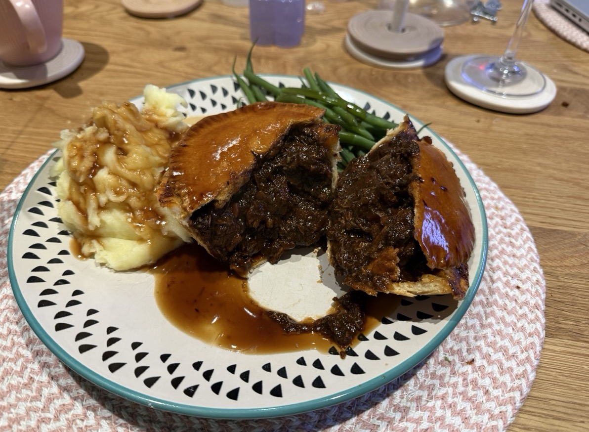 A dished up braised beef pie with mash and green beans