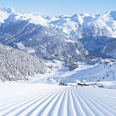 pistes de ski fraichement damées dans un paysage montagneux enneigé, sous un ciel bleu clair.