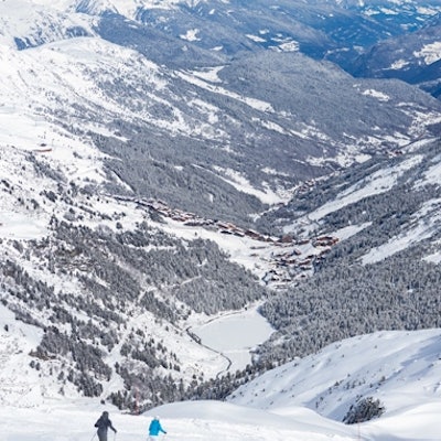 Paysage de montagne enneigée avec deux skieurs et un village en contrebas.