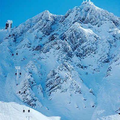Deux skieurs descendent une piste enneigée. En bas, un village est niché dans une vallée entourée de montagnes blanches.