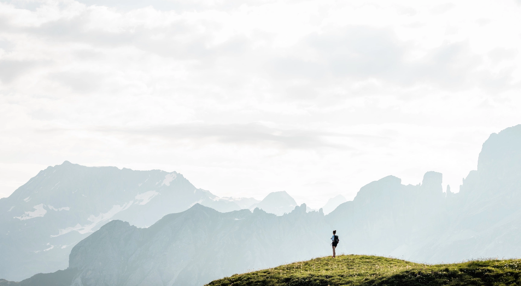 en 1er plan une personne en haut d'une montagne admirant les sommets en face d'elle