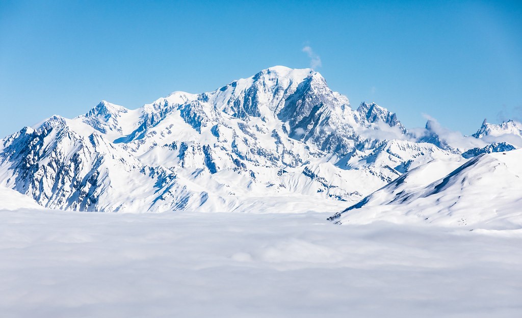 The legendary summit of Mont Blanc emerging from a sea of clouds under a blue sky