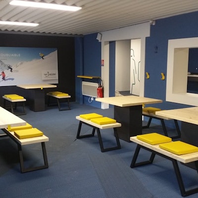 Modern break room with wooden tables and benches, yellow cushions. Blue walls, large photo of skiers, Wi-Fi access indicated.