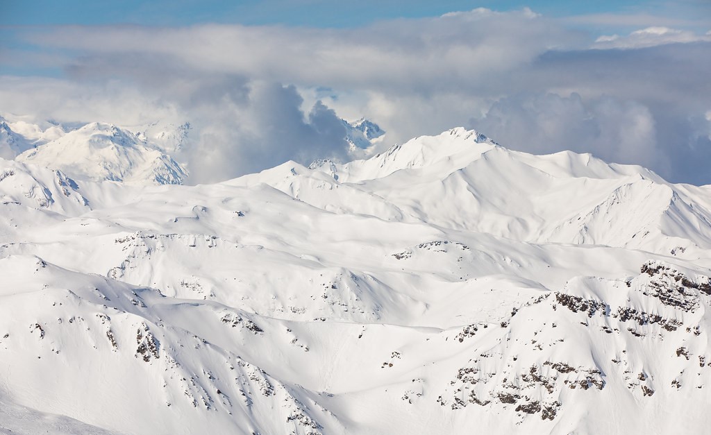 Snow-covered mountains under a cloudy sky, with some visible rocks.