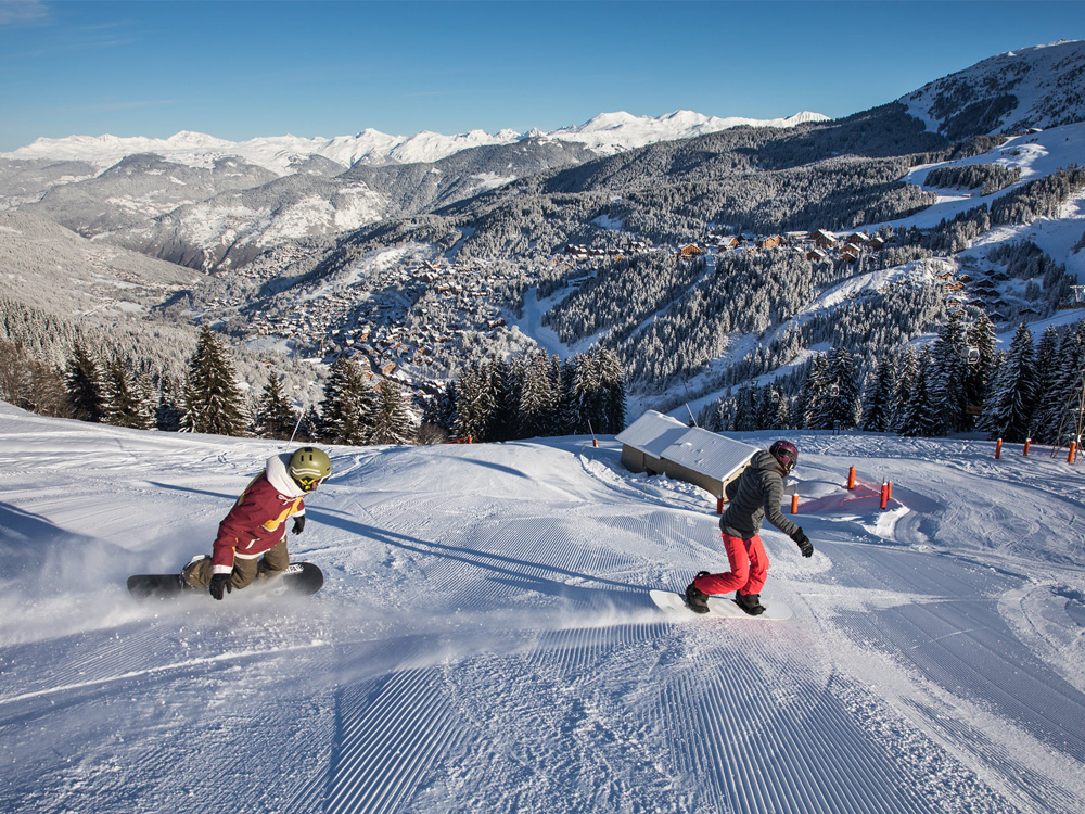 Two snowboarders descending a slope in Méribel