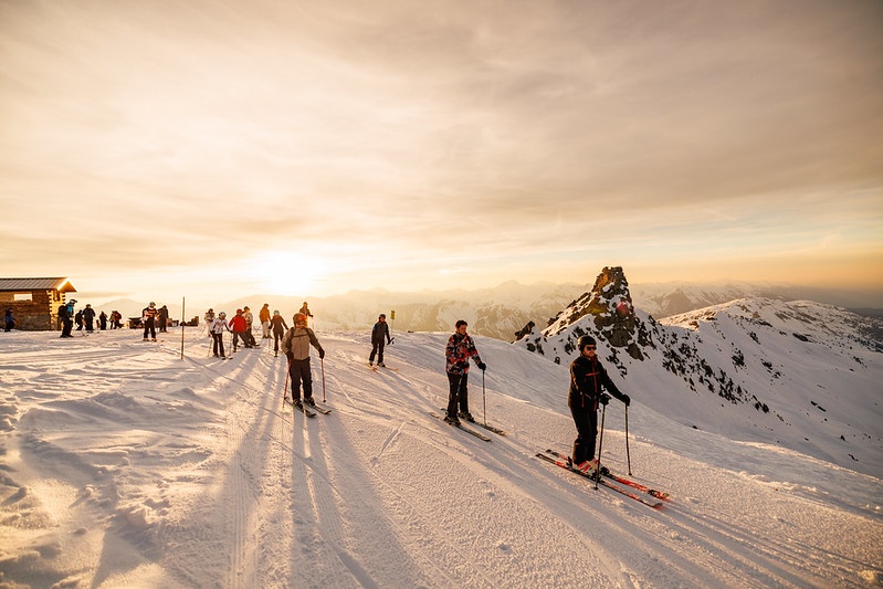 Un groupe de skieur entame la descente d'une piste enneigée sous le soleil couchant