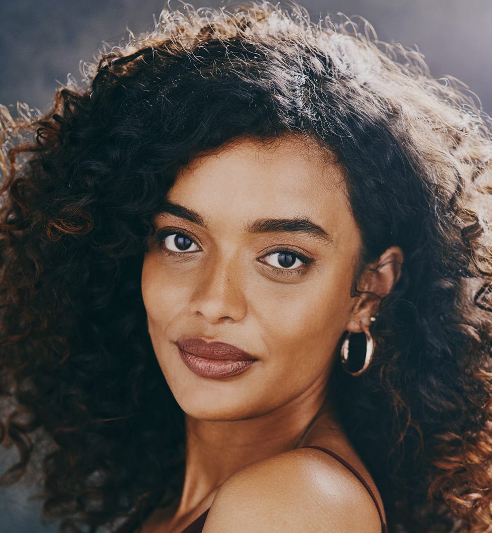 woman with a large curly hair and gold hoop earings posing for a picture