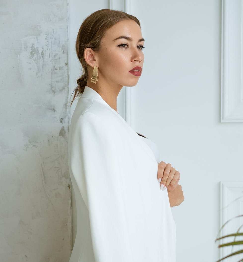 woman in white coat and earrings standing in front of a wall