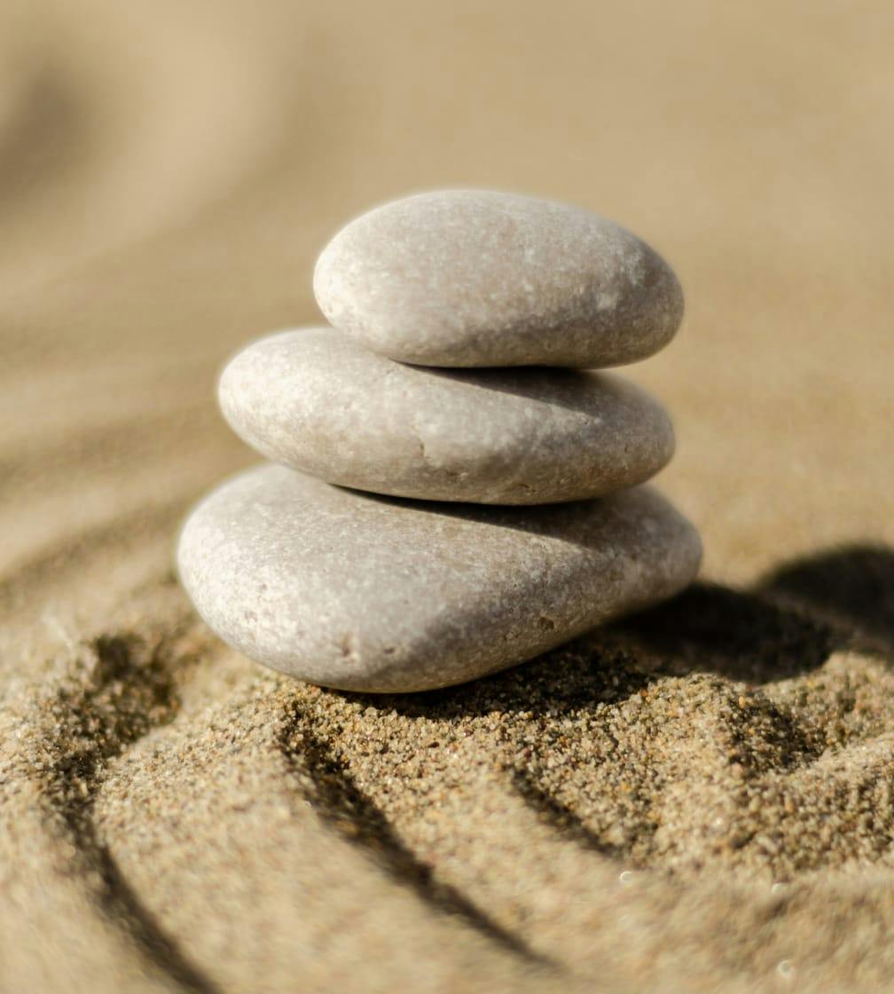3 zen river rocks stacked on top of each other on sand