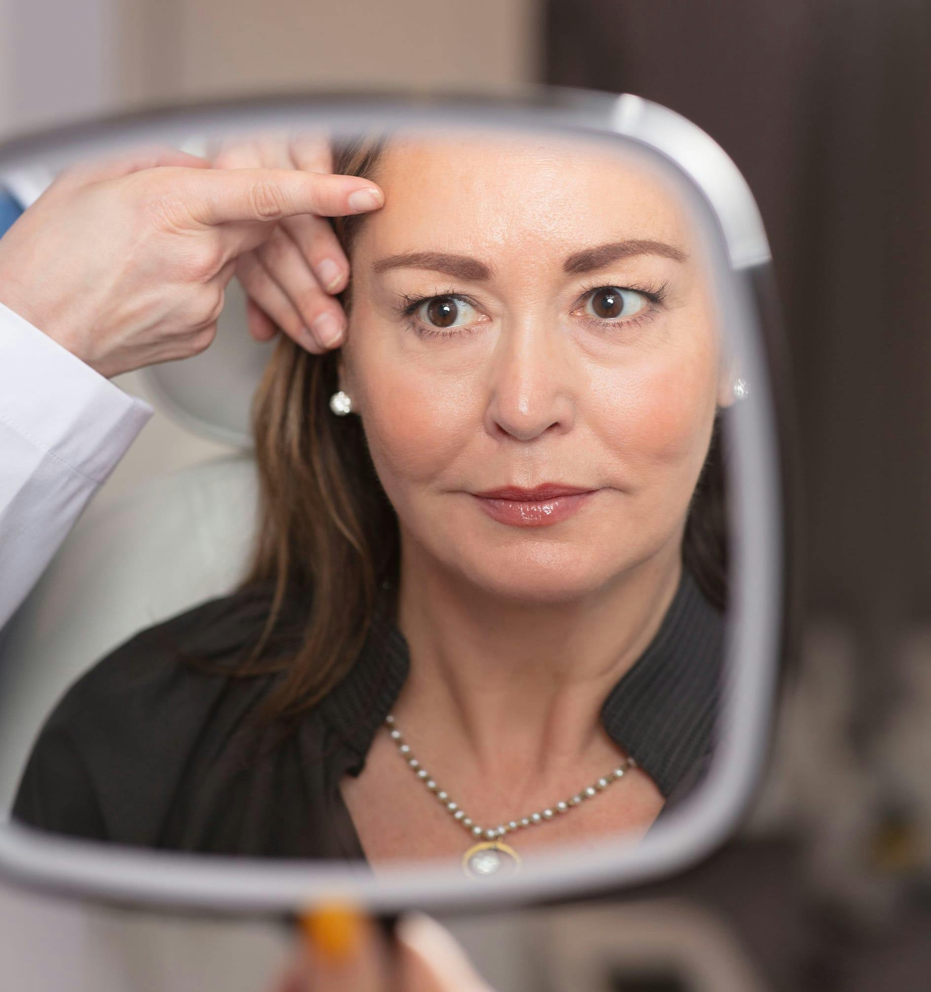 woman in mirror with doctor pointing to her face
