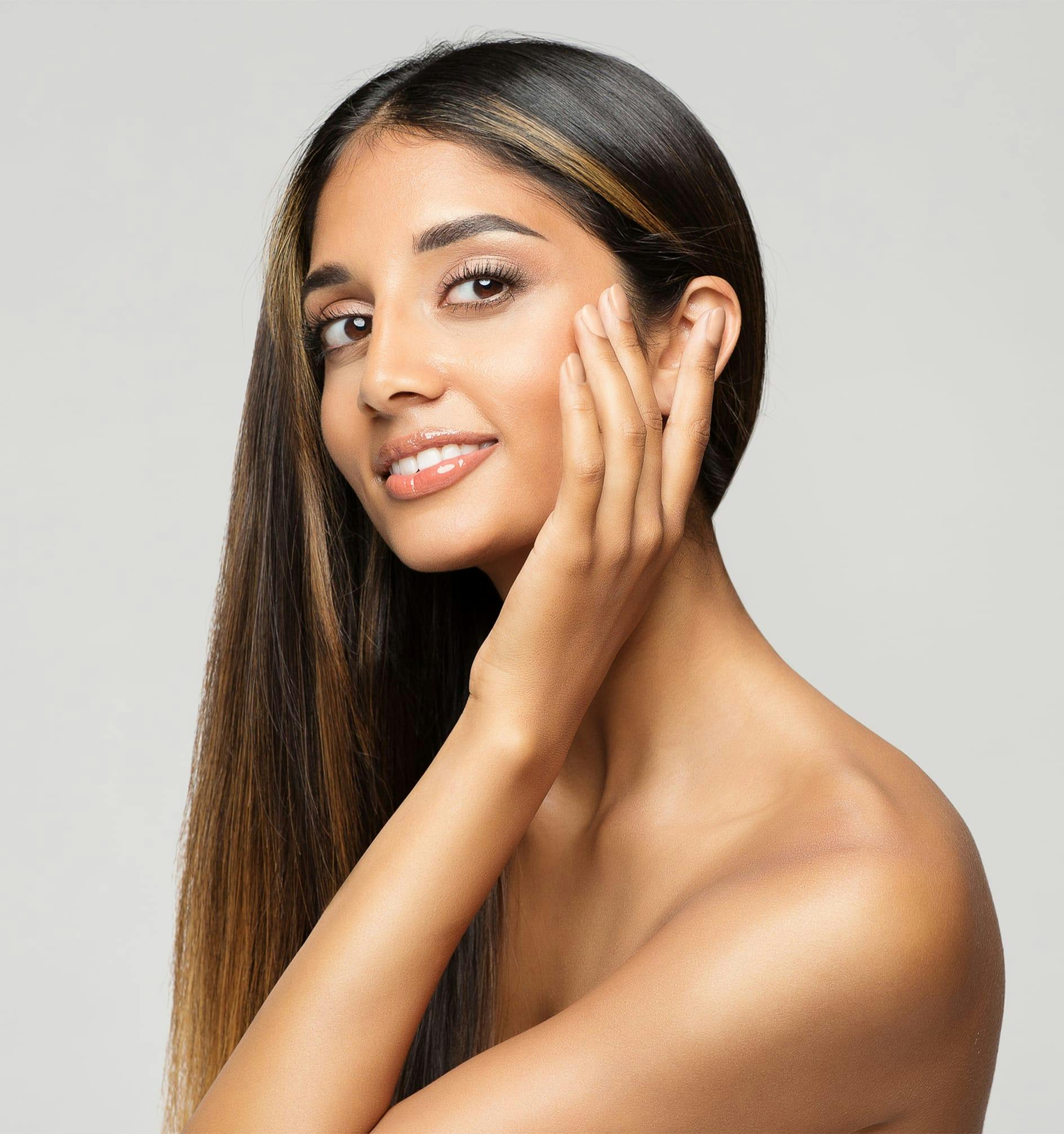 woman with long brown hair touching her face