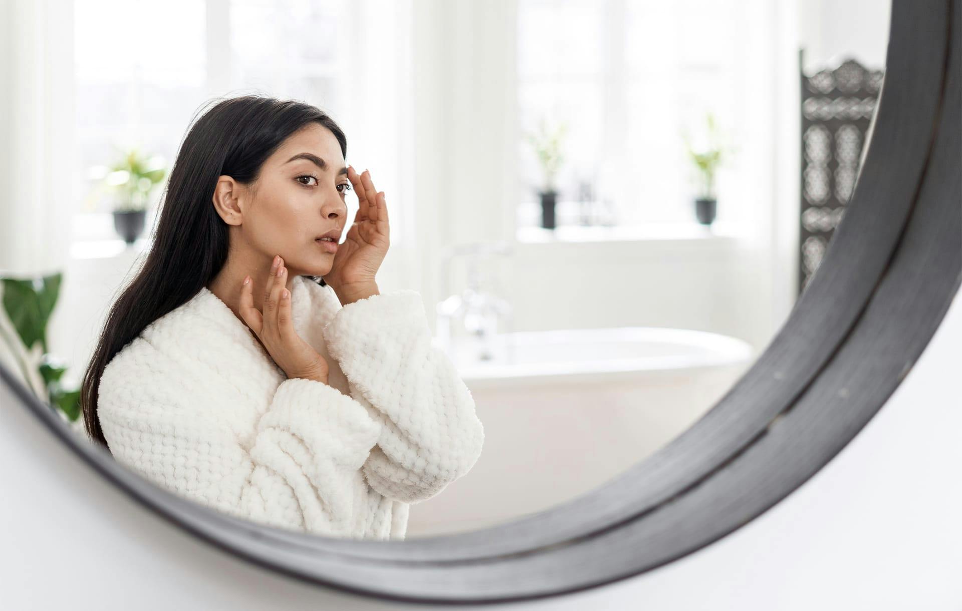woman looking in mirror touching her face