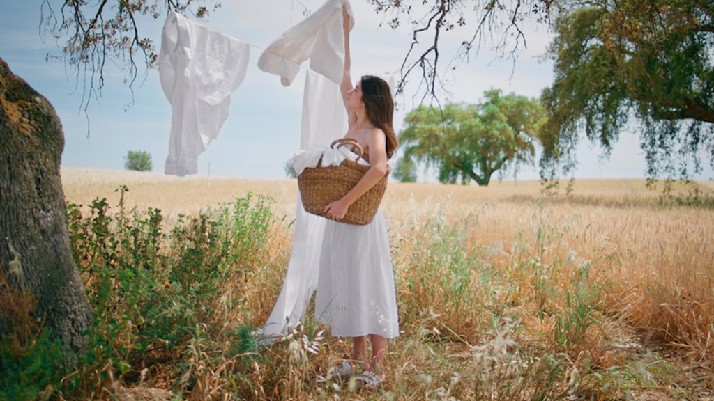 Vrouw in witte jurk die witte was ophangt in een mooi veld.