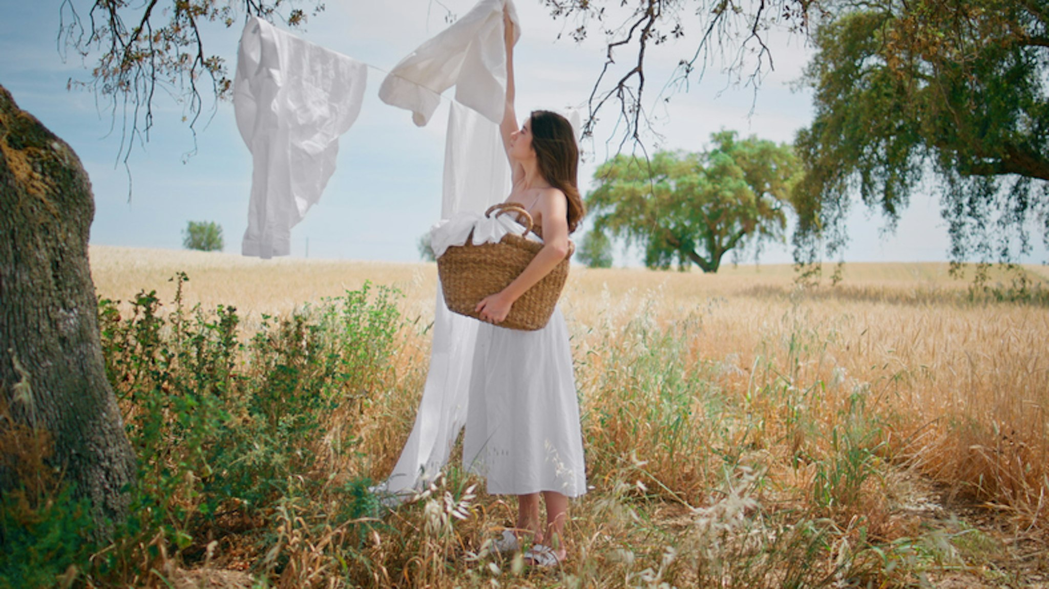 Vrouw in witte jurk die witte was ophangt in een mooi veld.