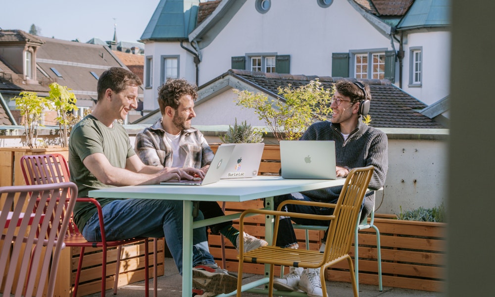 Drei Mitarbeiter von smartive sitzen mit ihren Laptops auf der sonnigen Dachterrasse von smartive in St. Gallen
