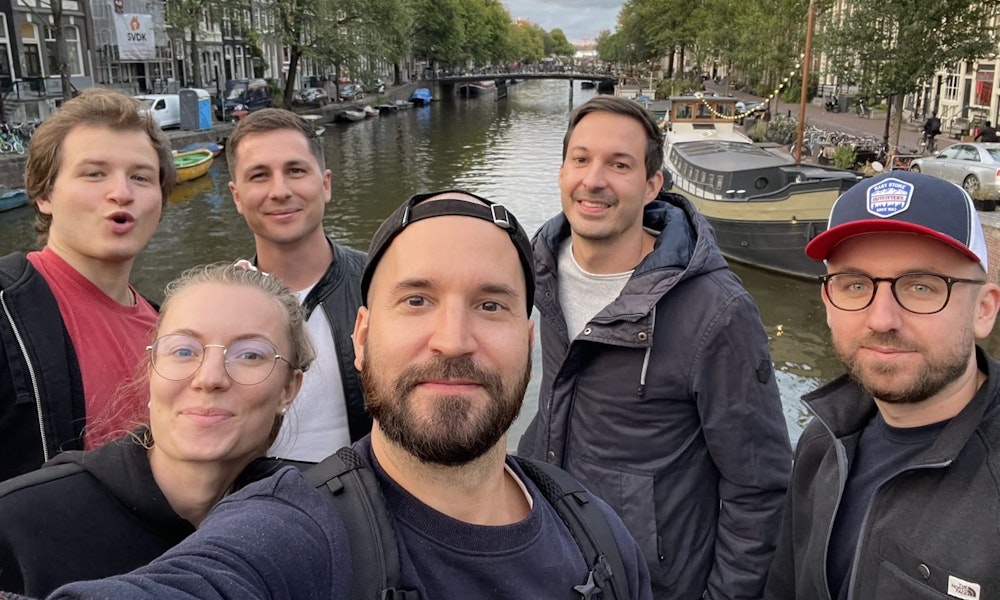 Eine Gruppe Menschen macht einen Selfie in Amsterdam mit einem Fluss im Hintergrund.