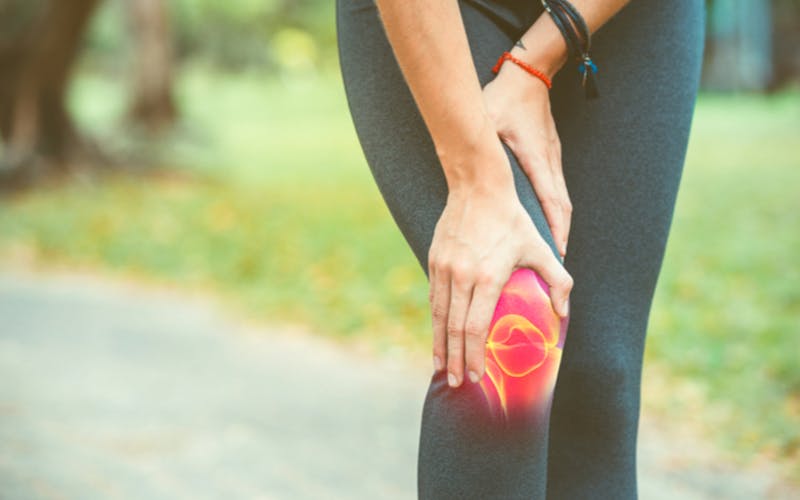 person touching their knee in pain while on a run