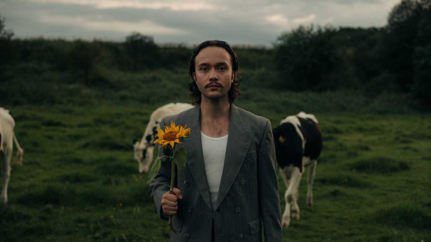 Magician standing in a field holding a flower in front of cows.