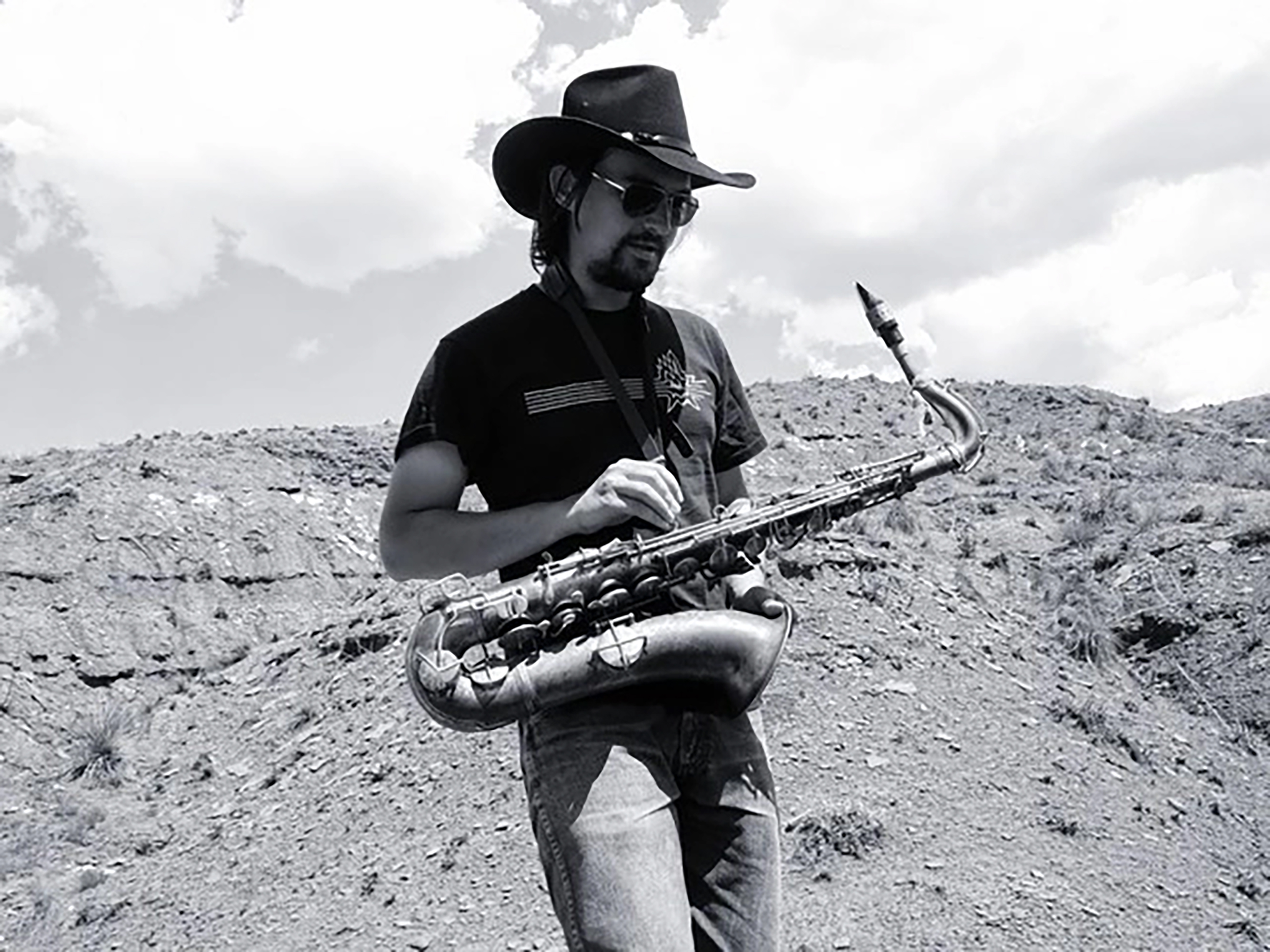 Svartvit bild på John Dikeman med saxofon i ett kargt landskap.