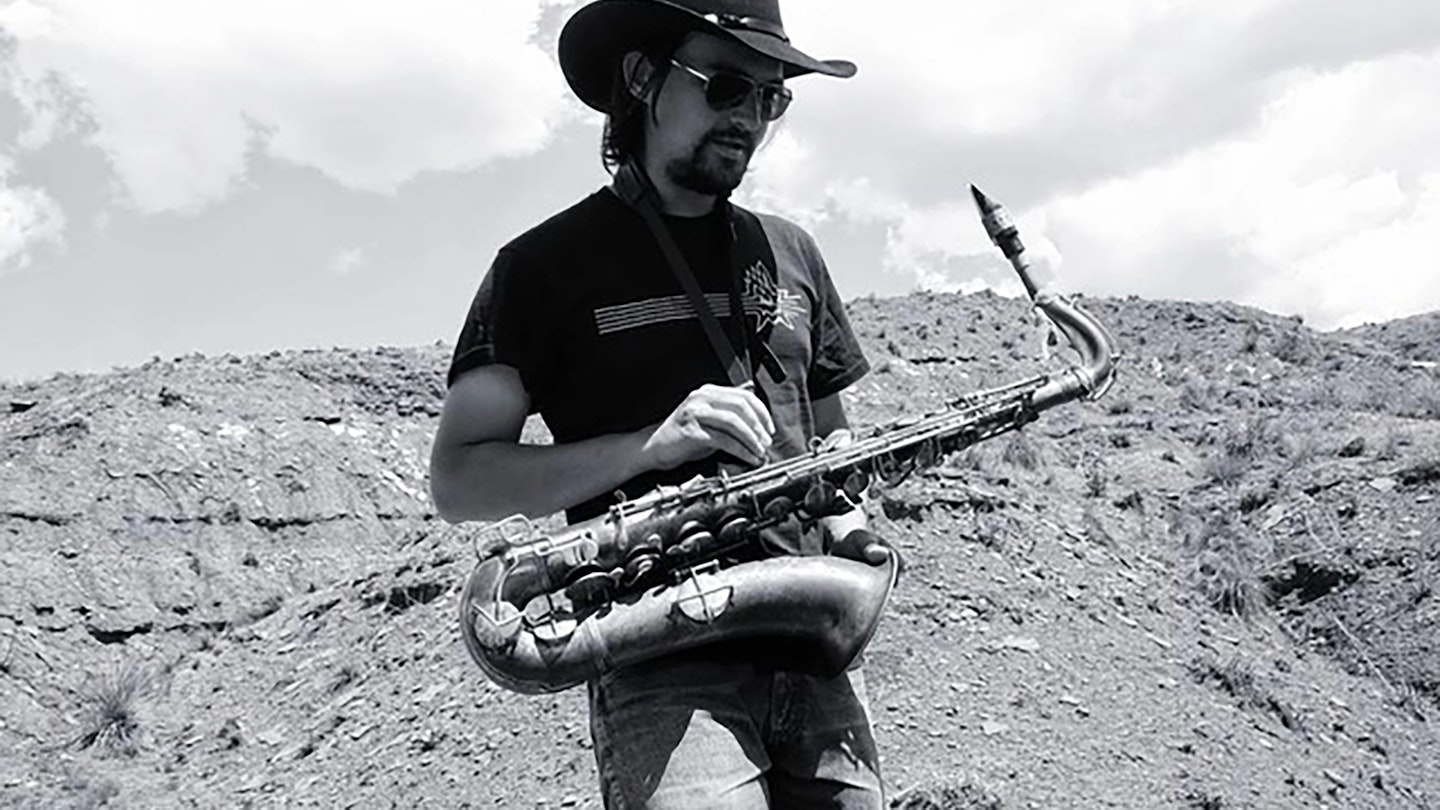 Svartvit bild på John Dikeman med saxofon i ett kargt landskap.