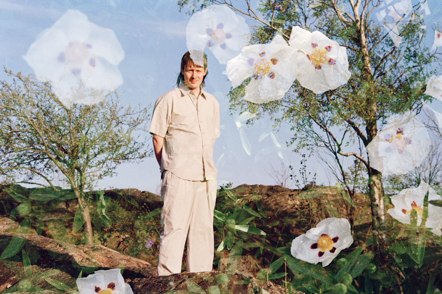 Bilden visar Jjulius i ljusa kläder ståendes ute i naturen. I bilden har vita blommor klippts in.