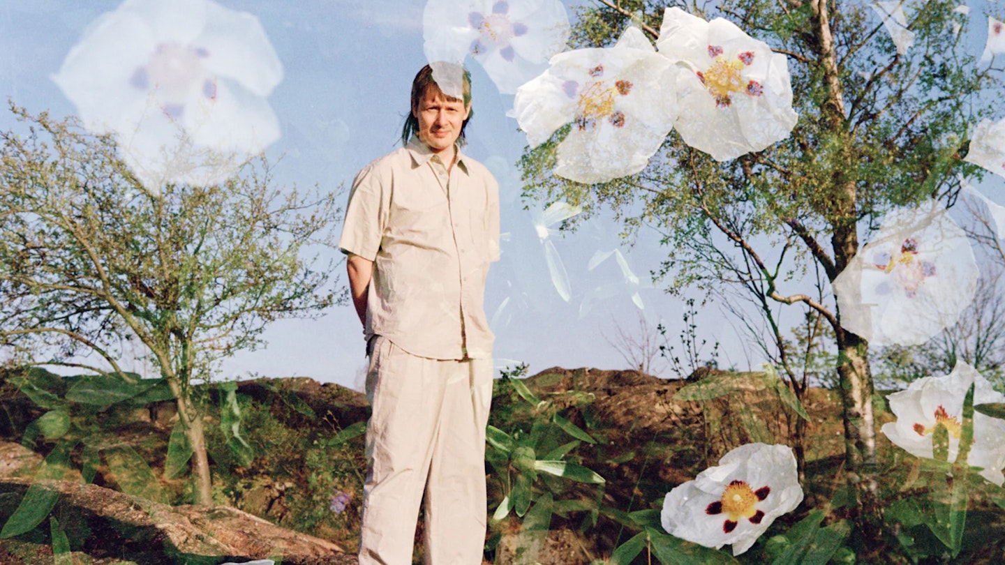 Bilden visar Jjulius i ljusa kläder ståendes ute i naturen. I bilden har vita blommor klippts in.