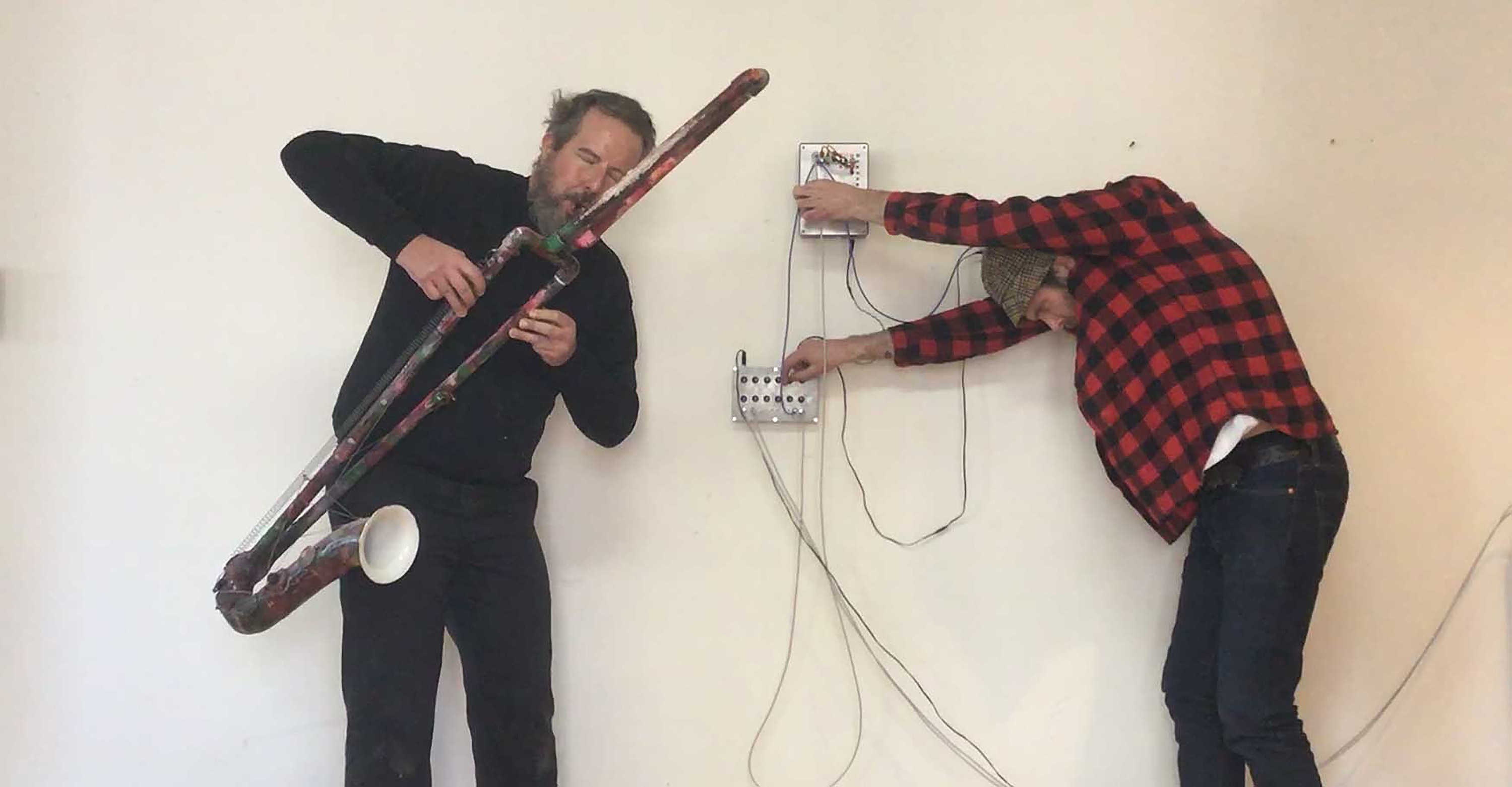 På bilden syns en person med ett blåsinstrument och en person som står böjd med sladdar mot en vägg.