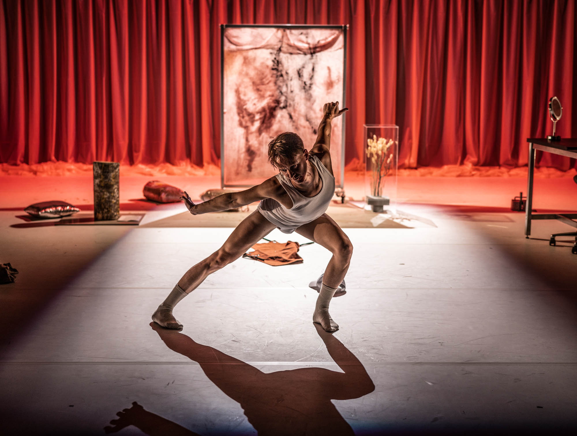 Skådespelare och dansare Olof Yassin i en rörelse. I bakgrunden syns en skärm med abstrakt motiv, samt röda draperier.