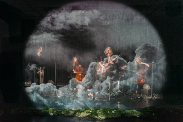 Fyra musiker sitter och spelar i en dimmig miljö.