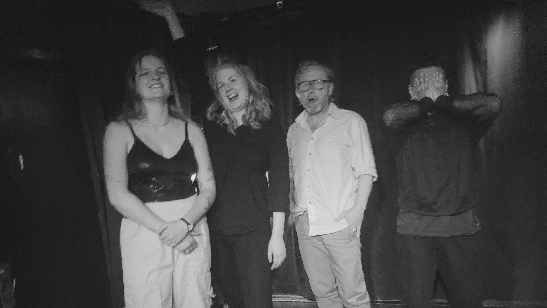 Svartvit bild med tre glada personer och en person som håller för ansiktet.